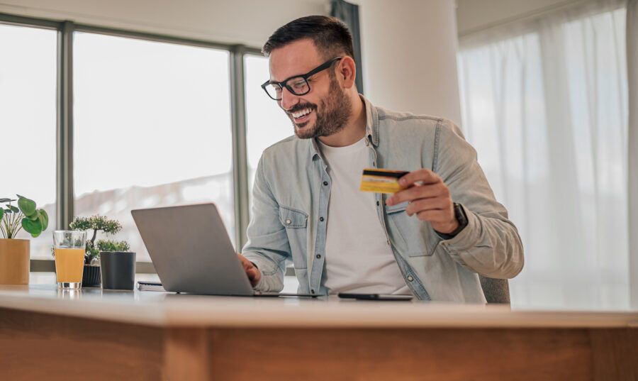 Smiling man using credit card and laptop, researching APR.
