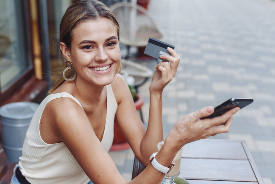 Smiling woman holding a payroll card outdoors at a cafe.
