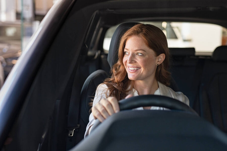 A woman driving smiles while looking outside her car window.
