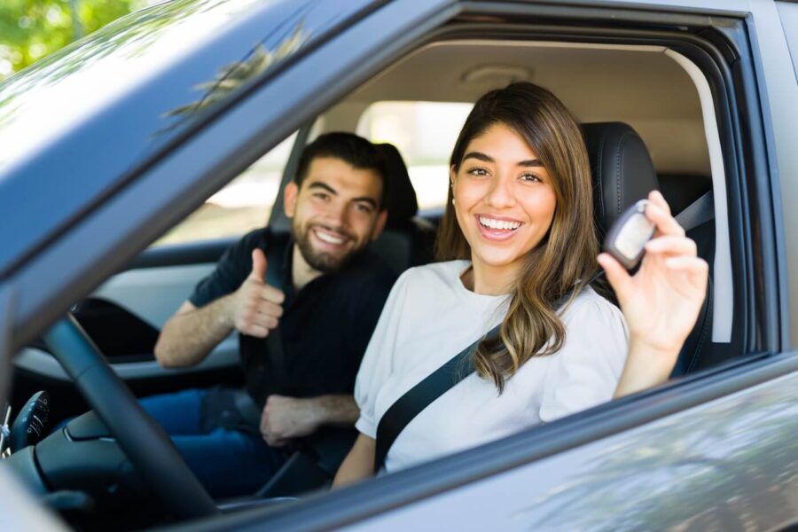 Happy young couple sitting in a new car, a woman holding the car keys