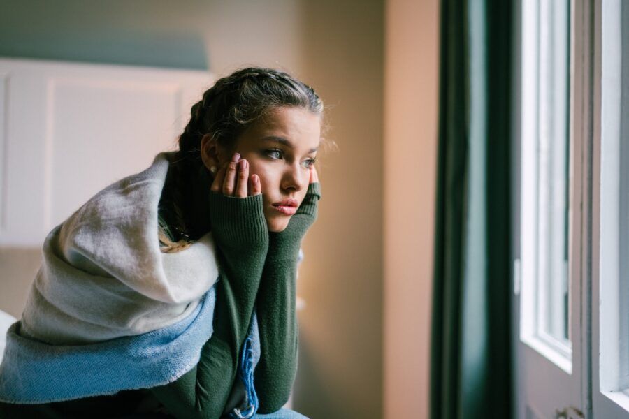Young sad woman sitting on her bed and looking through the window