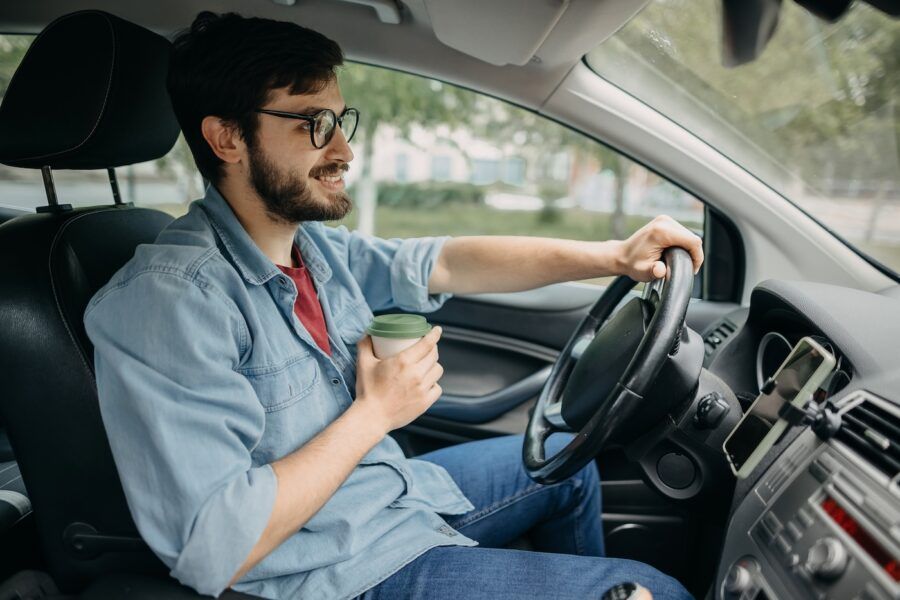 Young casual man driving car and drinking coffee on the way to work.
