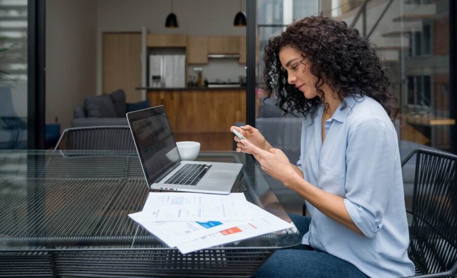 Woman checking her smartphone while working on her laptop