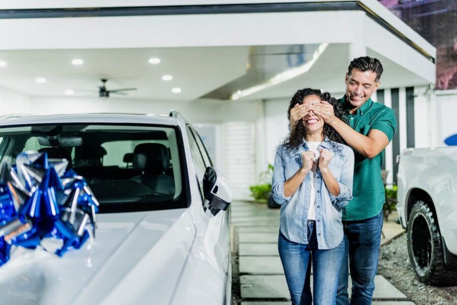 Man gifting a new car to his wife at dealership