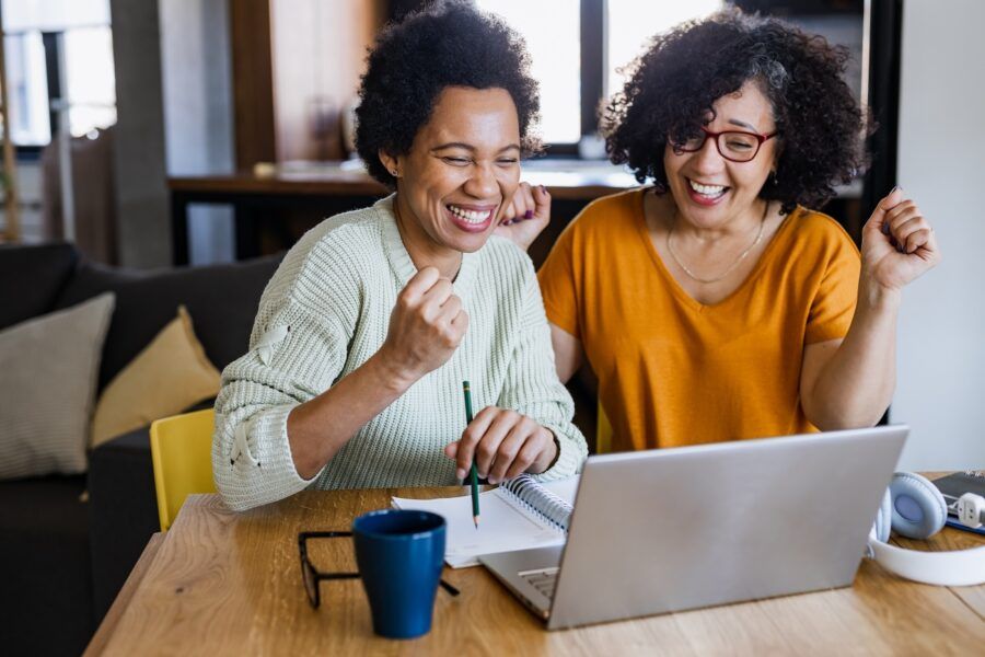 Two happy women are using a laptop to track their financial new years resolutions.