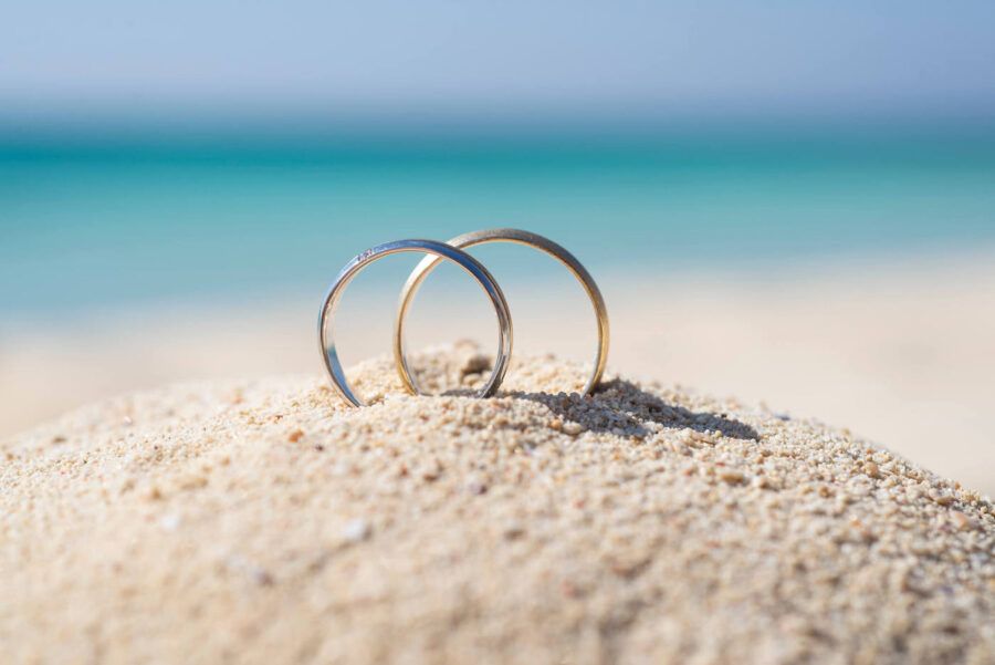 Two wedding bands standing upright in sand.