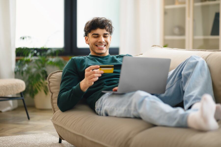 A man laying on the couch using his credit card and a laptop.