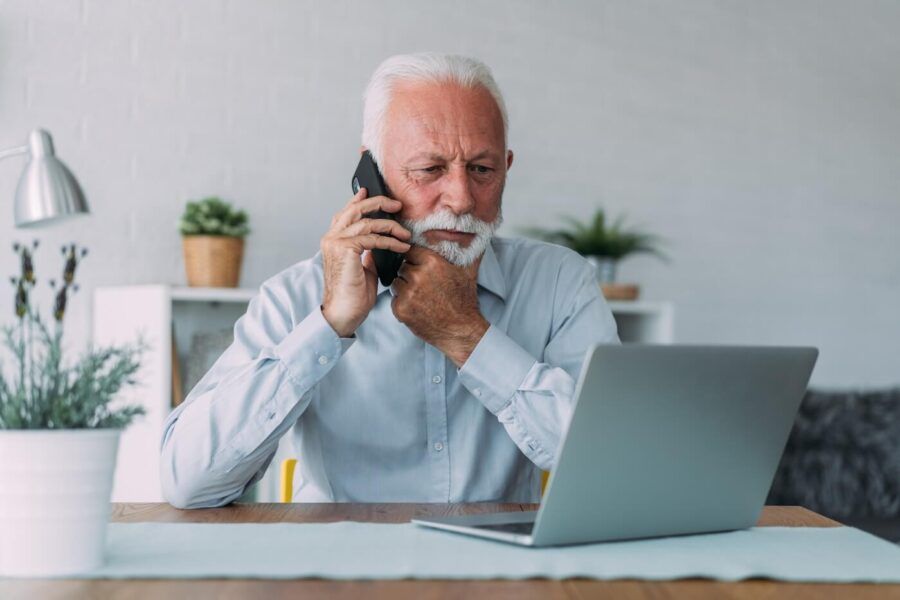 Concerned senior man making a phone call while looking at his laptop