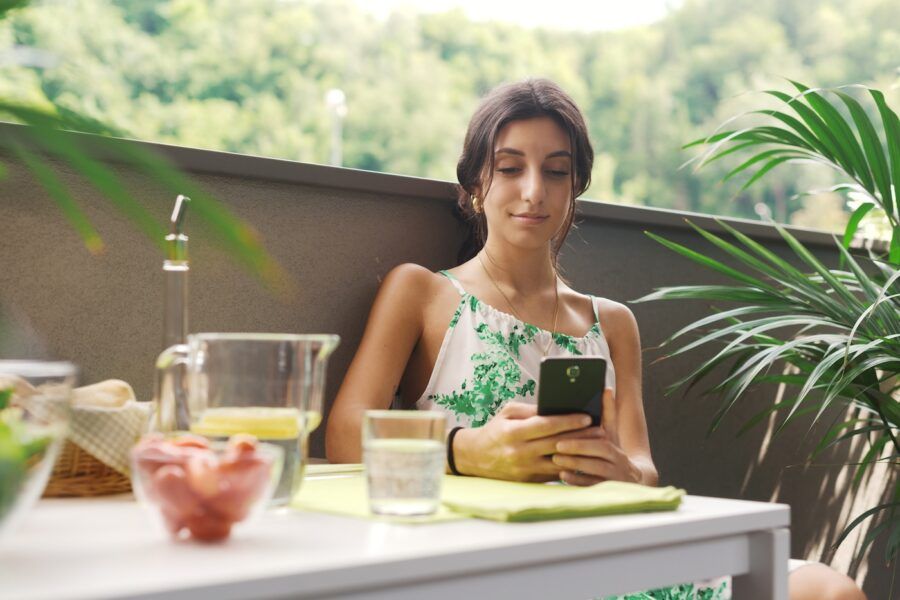 Young happy woman relaxing on the balcony and using her smartphone.