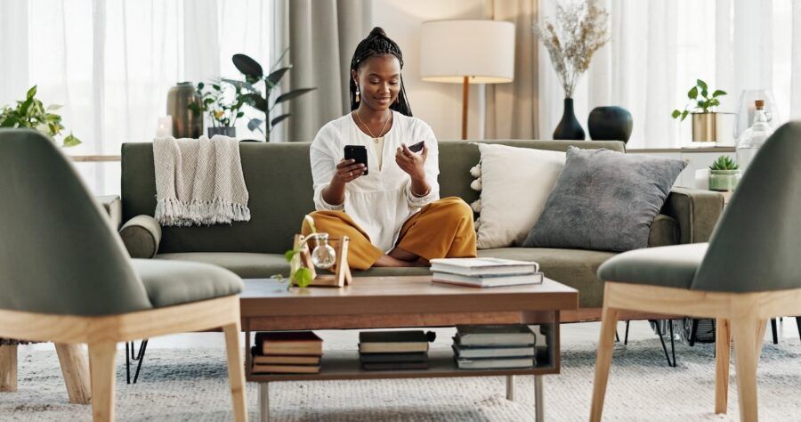 A woman sitting on her couch at home with her credit card and phone.