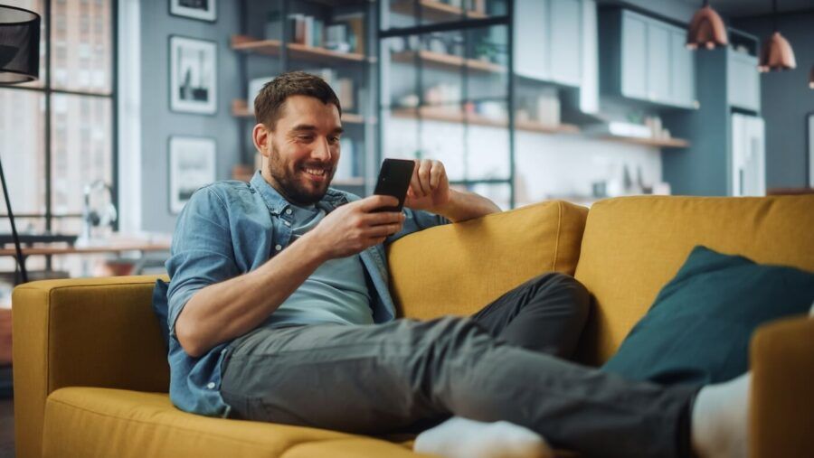 Smiling man relaxing on the sofa while using his smartphone