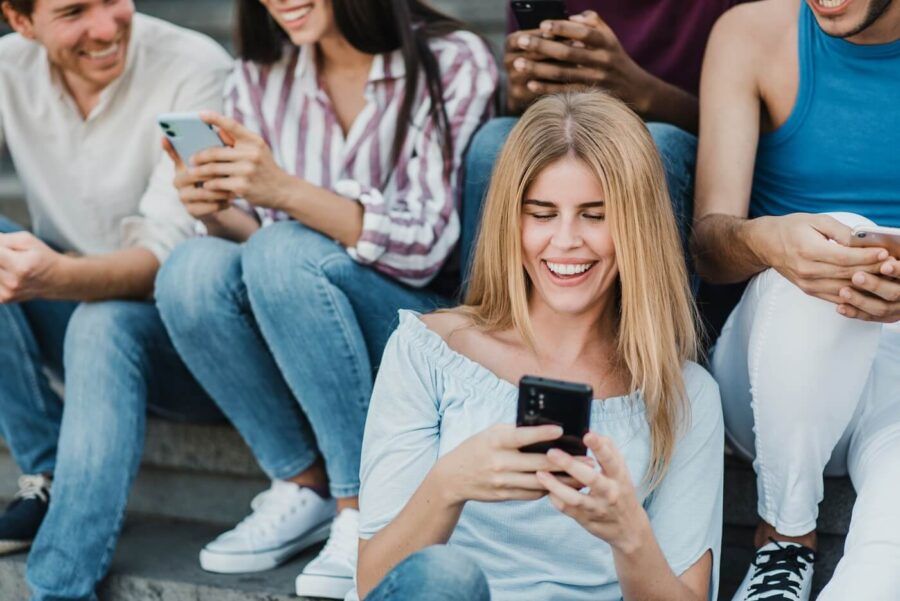 A group of people sitting close together on outdoor steps, all holding smartphones, with a young woman in the foreground looking at her phone.