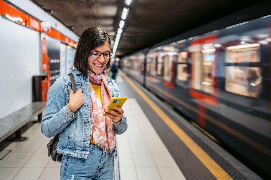 A young woman using smart phone in a subway station while waiting for her train.