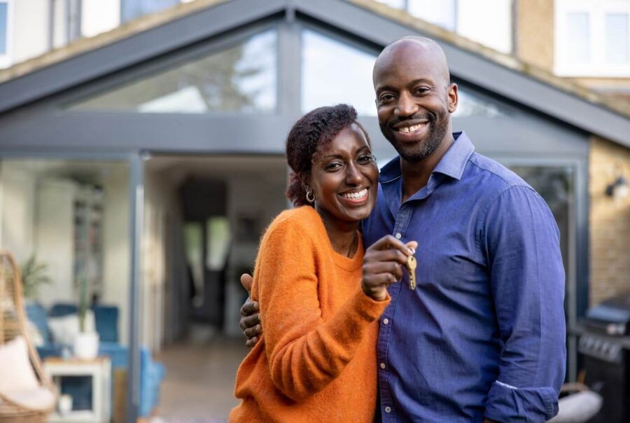 Cheerful couple standing outside of their new house and holding the keys