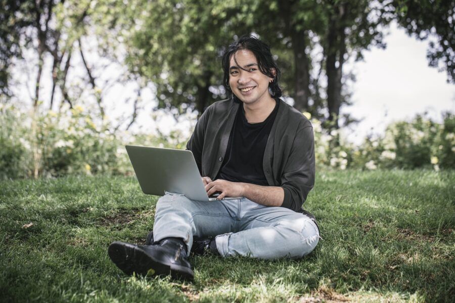 A young man in his twenties works with his laptop in a park in springtime.