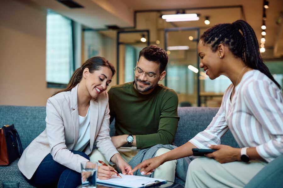 Happy woman signing a contract next to a man during a meeting with real estate manager in her office.