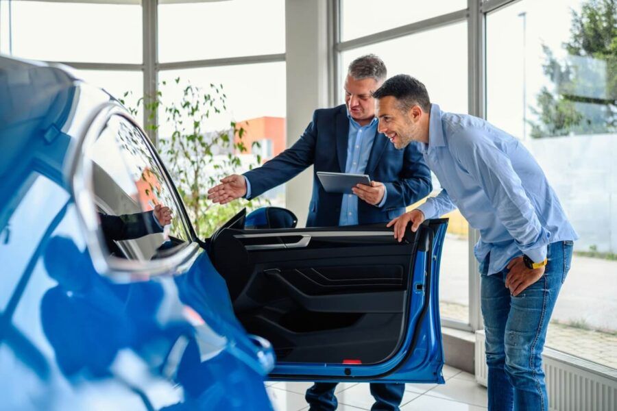 Male dealership agent is showing the blue car interior to a smiling male customer
