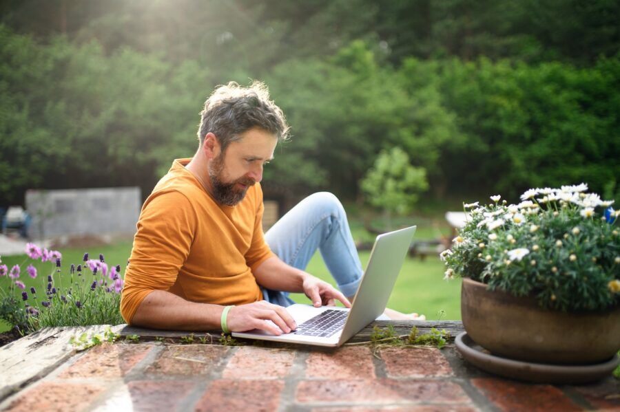 Happy mature man with laptop working outdoors in garden.