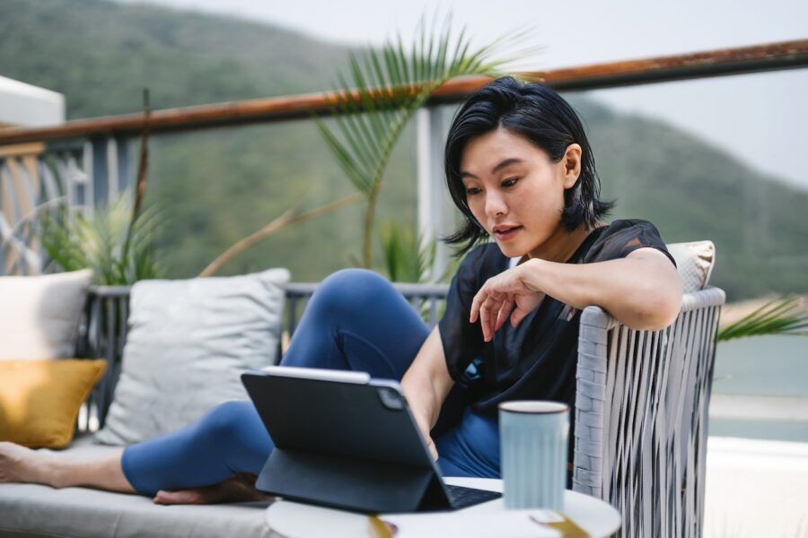 Young woman sitting on the balcony, using digital tablet and having a cup of coffee in the