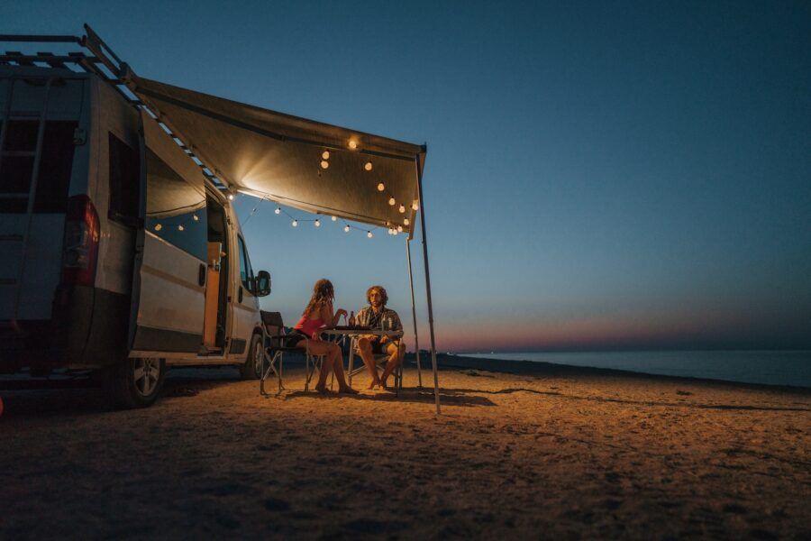 Young couple sitting outside their RV parked on the beach at sunset.