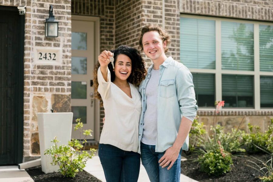 Happy young couple standing next to their new house, the woman is holding the house keys
