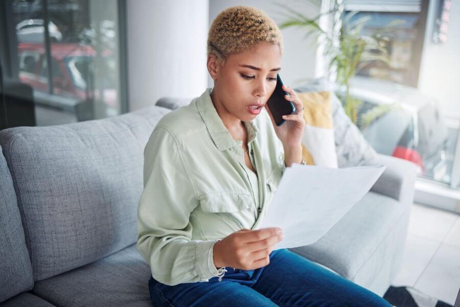 Concerned young woman making a phone call while reviewing printed documents.
