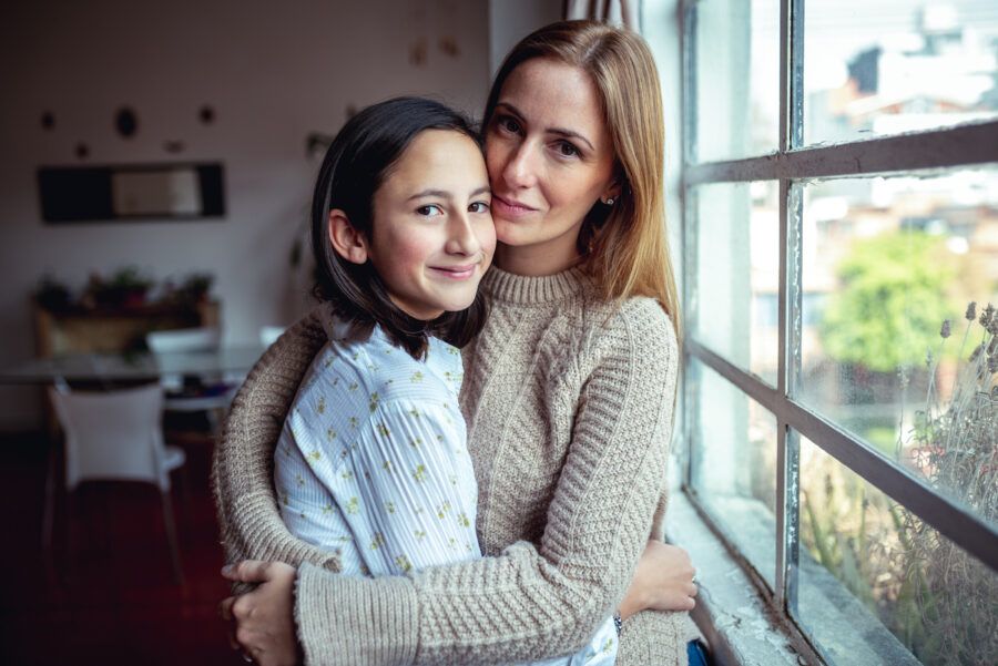 A mother and daughter hugging and looking at the camera.