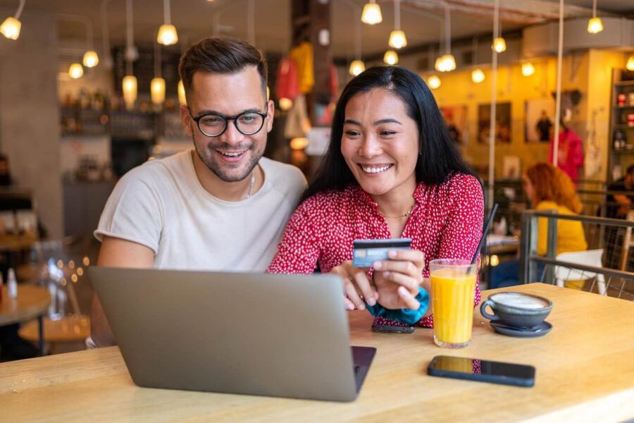 Happy couple using laptop in the cafe, the woman is holding a credit card