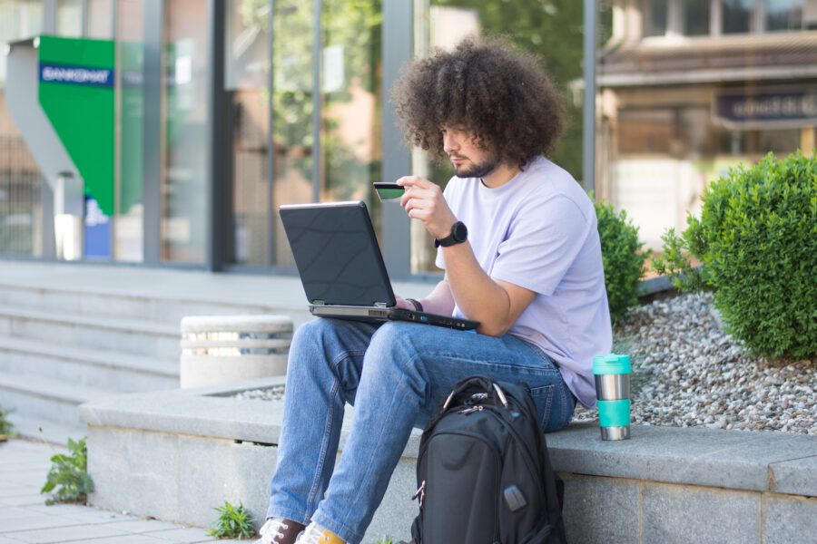 Young man sitting outdoor and using laptop and credit card