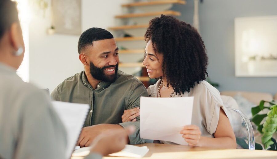 Happy couple sitting in a lender’s office, holding printed documents