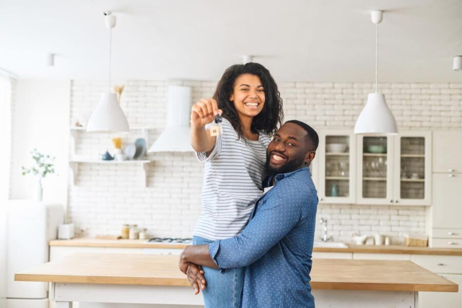 Happy couple standing in the kitchen; the man is lifting the smiling woman who is holding the keys