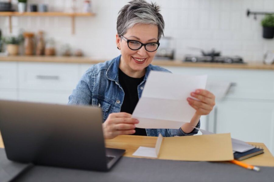 Mature woman reading her mail while using her laptop at home.