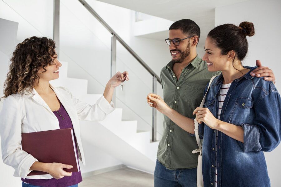 Medium shot of couple receiving keys from real estate agent while standing in new empty apartment during daytime.