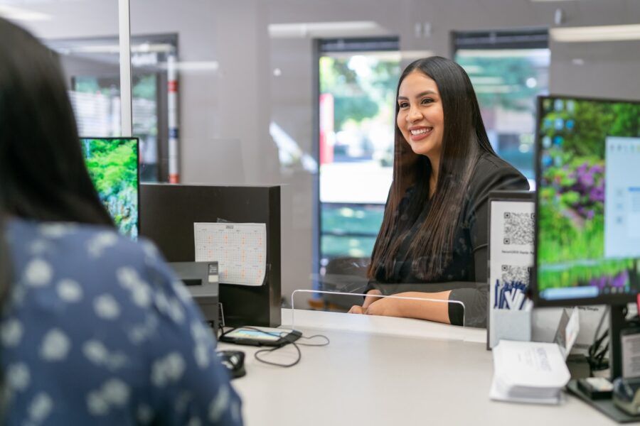 A cheerful woman smiles while talking to a bank receptionist.