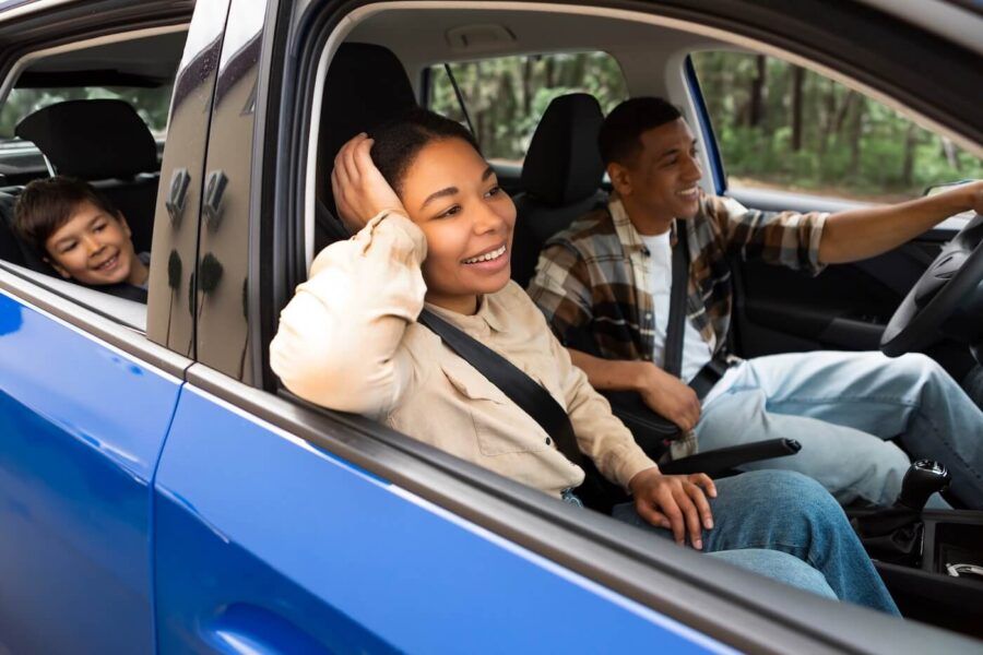 Happy family of three on a road trip, driving with open windows