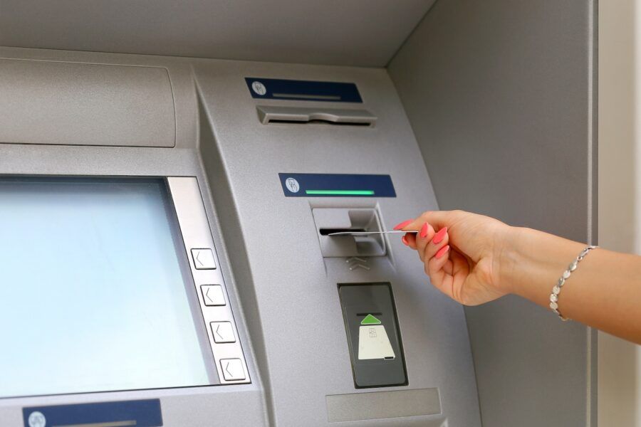 A woman's hand with red nails inserting credit card to ATM.