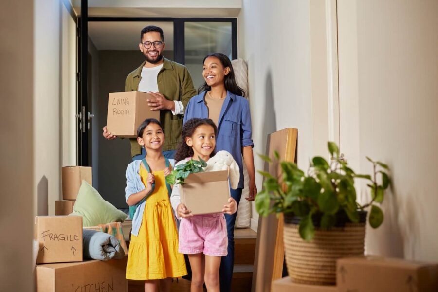 Happy family of four with two young daughters entering their new house with moving boxes in hands