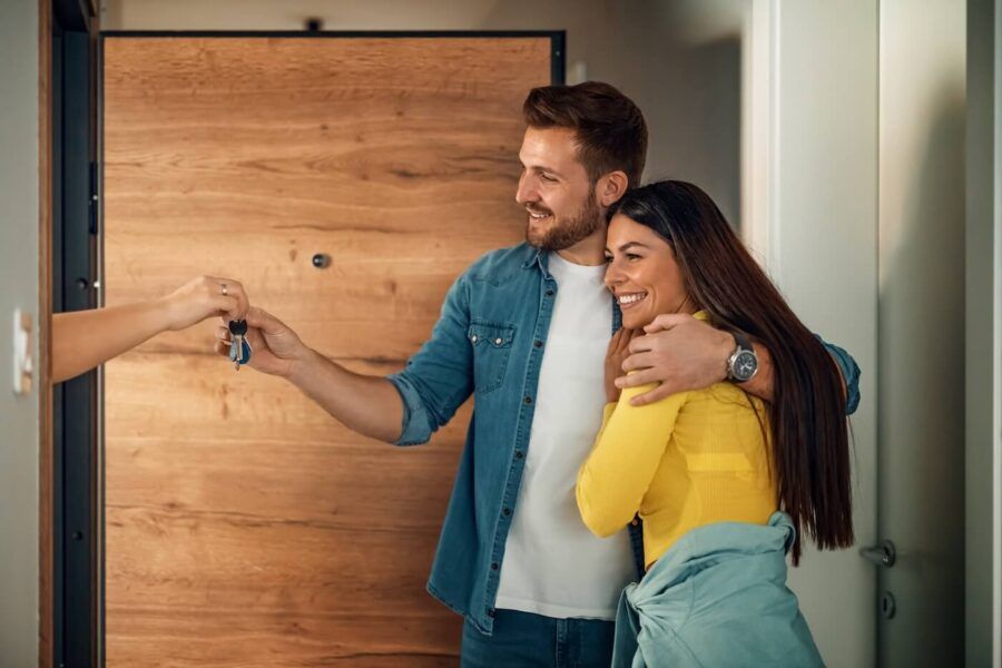 Happy couple hugging each other, the man taking the house keys from someone behind the front door