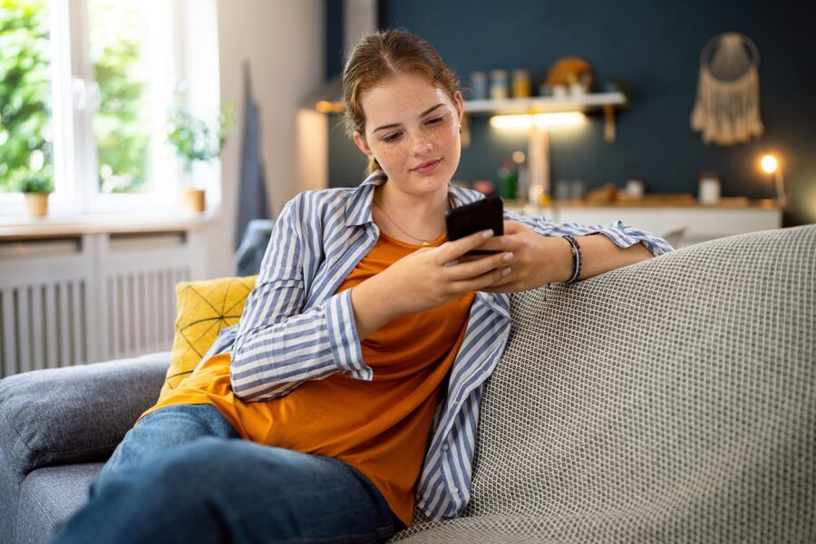 Woman using mobile phone while sitting on the sofa in the living room.