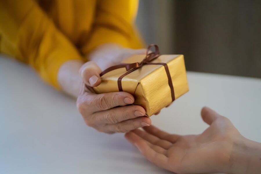 A yellow gift box being passed from one set of hands to another.