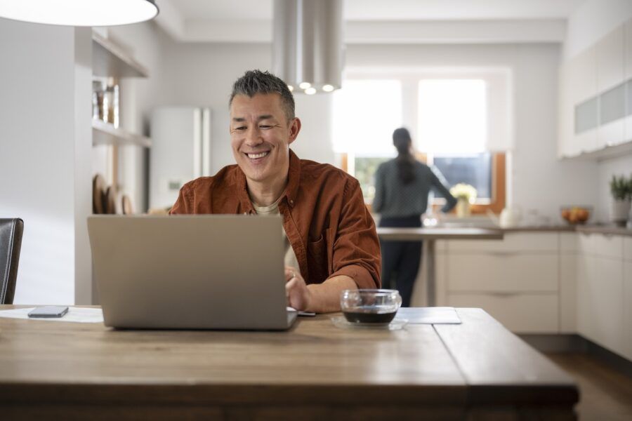 Mature man working on laptop while sitting at dining table at home.