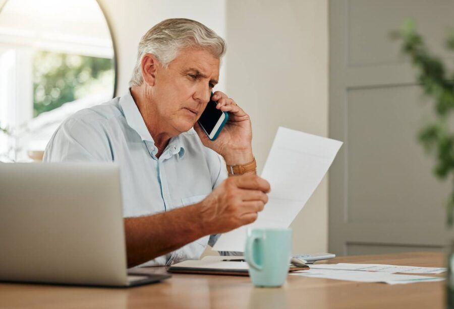 A concerned senior man is holding a paper while making a call