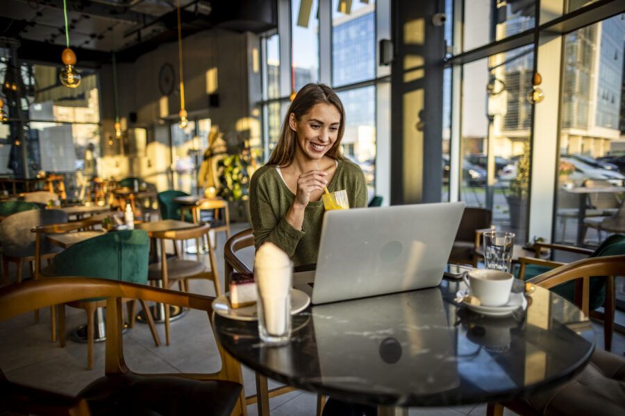 Smiling young woman sitting in cafe and looking at investments on a laptop.