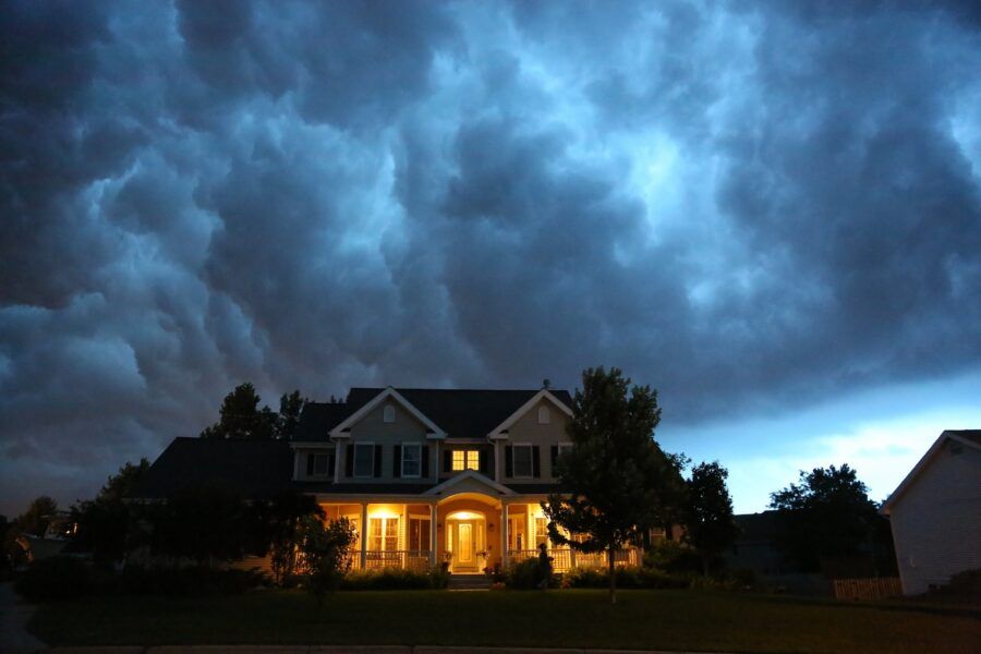 A house is lit up while a large thunderstorm moves in overhead at dusk.