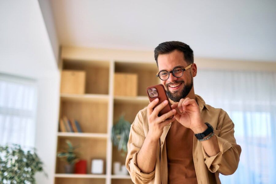 Smiling young man using his smartphone at home