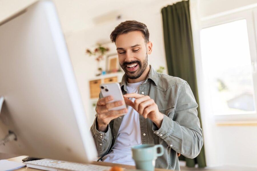 Happy young man checking a smartphone in his home office