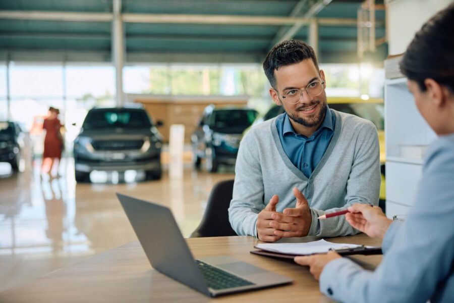 Young man discussing car purchase details with a saleswoman in a showroom, preparing to sign a contract for a new vehicle.