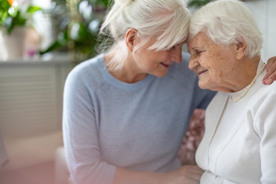 Two senior women, likely mother and daughter, embracing warmly and smiling at each other.