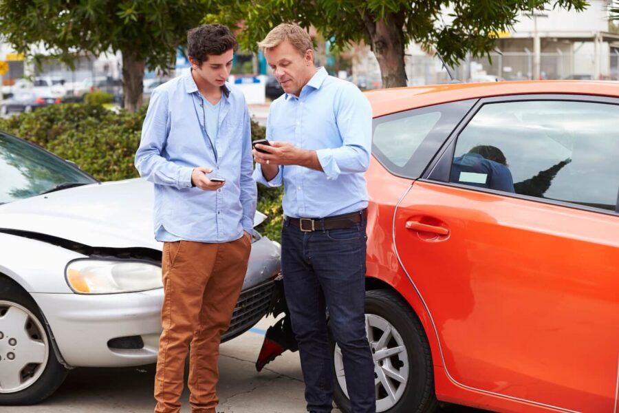 Two men are standing next to their cars and exchanging contact information after a minor car accident