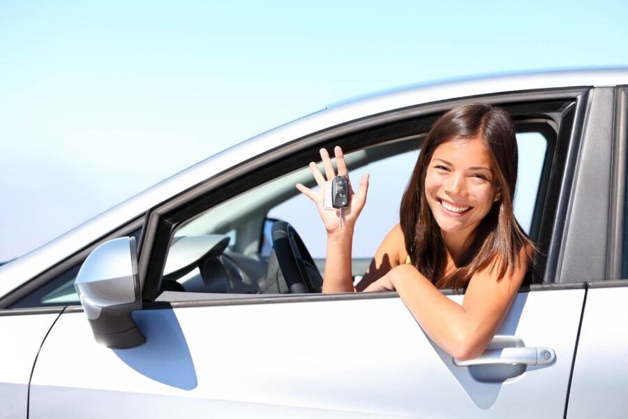 Smiling young woman sitting in the white car and holding the keys